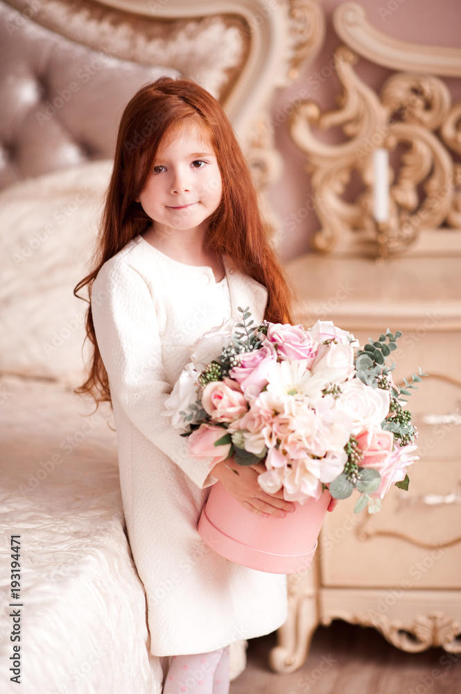 Smiling baby girl 4-5 year old holding flowers wearing white jacket in room. Looking at camera. Spring season. Smiling baby girl 4-5 year old holding flowers wearing white jacket in room. Looking at camera. Spring season.