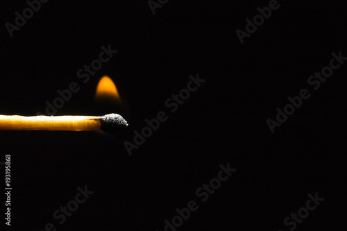 Burning match stick in the left corner of the frame on a black background 