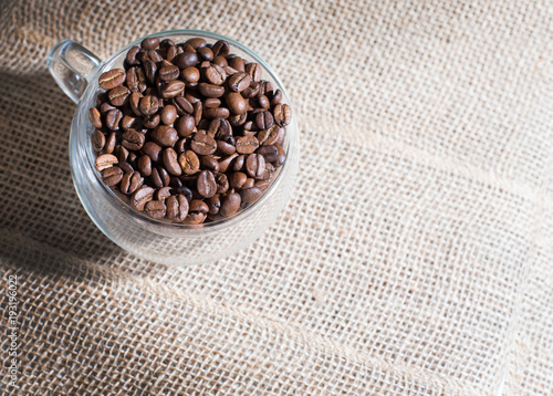 Artistic coffee themed background: a glass cup full of roasted beans on a burlap
