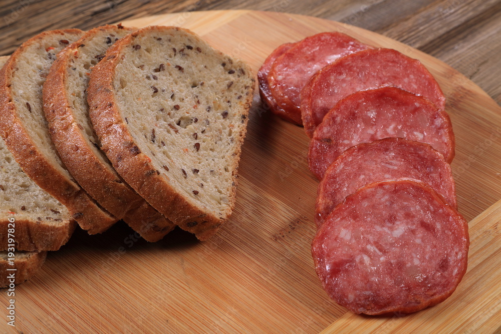 On the cutting board is sliced bread and sliced sausage. A table of an old tree. On the cutting board is sliced bread and sliced sausage. A table of an old tree.