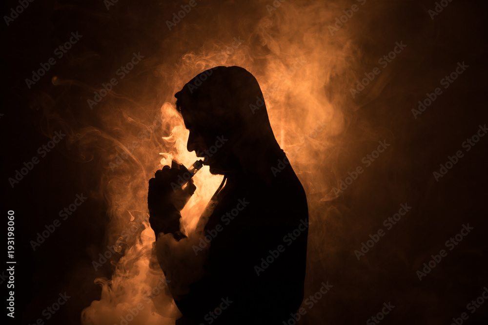 Vaping man holding a mod. A cloud of vapor. Black background. Vaping an electronic cigarette with a lot of smoke. Vape concept