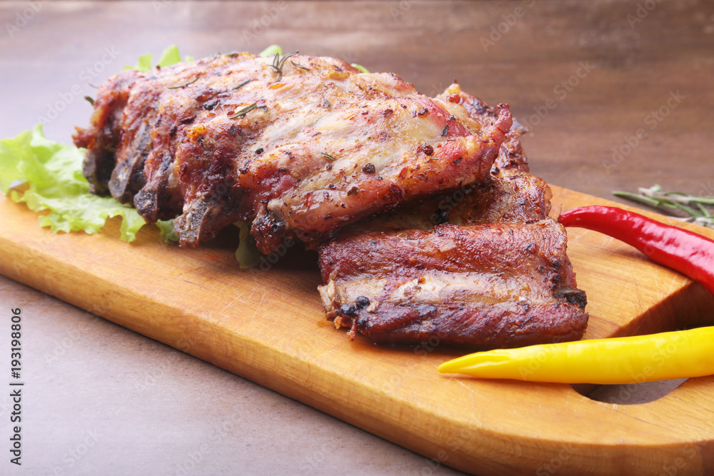 grilled barbecued ribs with lettuce leaves, hot chili pepper and sauce on wooden cutting board. grilled barbecued ribs with lettuce leaves, hot chili pepper and sauce on wooden cutting board.