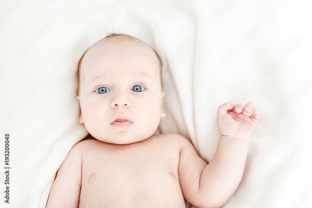 Funny cute little boy lying on a bed. Surprised and frightened emotion on child face. Waving a hand , hello world concept. Top view Funny cute little boy lying on a bed. Surprised and frightened emotion on child face. Waving a hand , hello world concept. Top view