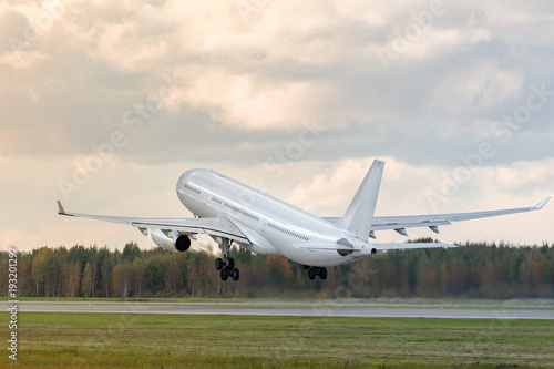 Beautiful wide-body modern passenger airplane fly up over take-off runway from airport, copy space/ Departure board / Low over the runway, back view/ Vacation, aviation, travel, trip - concept