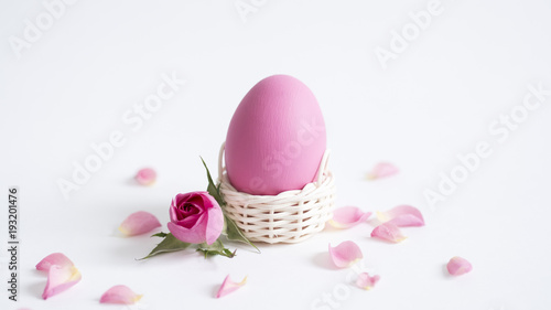 Easter greeting card with Easter egg and petals of pink roses on white background with copy space.