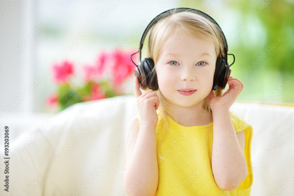 Cute little girl wearing huge wireless headphones. Pretty child listening to the music. Schoolgirl having fun listening to kid's songs at home. Cute little girl wearing huge wireless headphones. Pretty child listening to the music. Schoolgirl having fun listening to kid's songs at home.