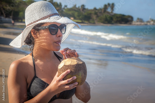 Latina woman on holiday drinking a coconut on the beach 
