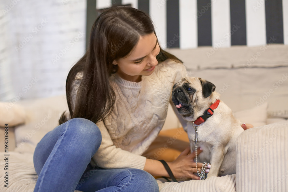 Young woman with cute pug dog on sofa at home. Pet adoption