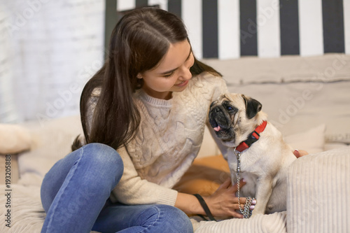 Young woman with cute pug dog on sofa at home. Pet adoption © Africa Studio