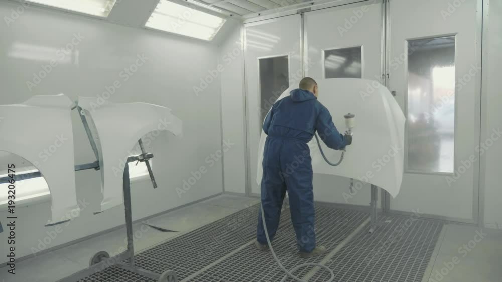 Auto painter spraying white paint on car hood in special booth Auto painter spraying white paint on car hood in special booth