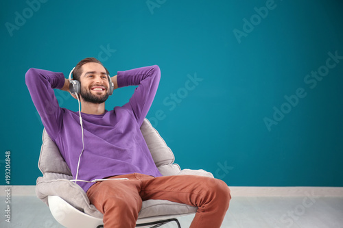 Foto Handsome man listening to music while sitting in comfortable armchair against co