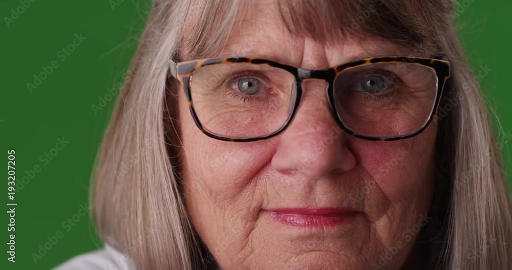 Tight shot of somber elderly woman wearing eye glasses in front of greenscreen Tight shot of somber elderly woman wearing eye glasses in front of greenscreen