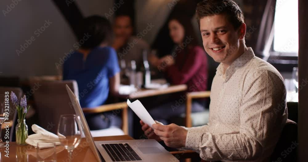 4K Portrait of attractive smiling restaurant manager working on laptop with customers in the background 4K Portrait of attractive smiling restaurant manager working on laptop with customers in the background