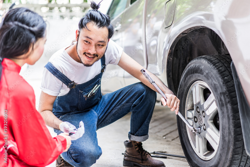Fixing car engine in automobile repair garage. Handsome mechanics in uniform are repairing car while working in auto service Fixing car engine in automobile repair garage. Handsome mechanics in uniform are repairing car while working in auto service