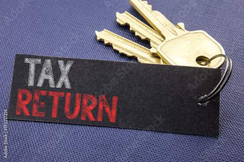 Handwritten text showing Tax Return. Business concept writing for Taxation Refund Written on note paper attached to the key, black background with space close up © Artur