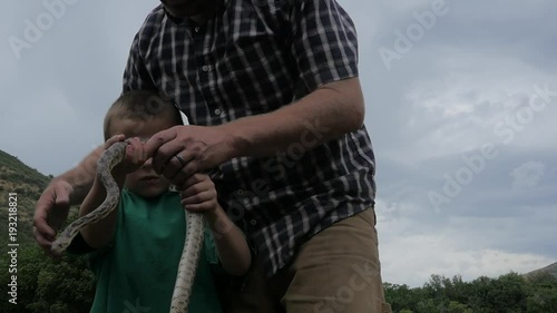 Father shows son a large snake and lets him hold it. photo