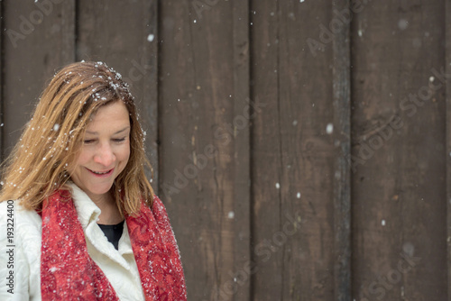 beautiful woman standing outside brown wood barn with fresh snow falling