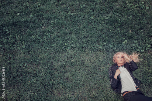 blonde lying on the grass. portrait of woman in fashionable black leather jacket. photo