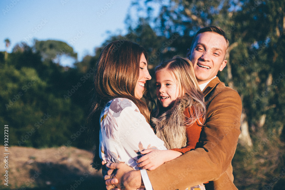 A smiling young dad hugging his wife and daughter A smiling young dad hugging his wife and daughter
