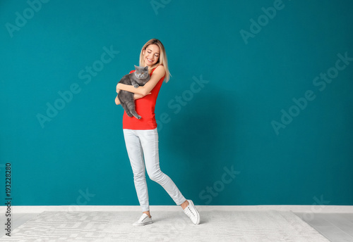 Young woman with cute pet cat against color wall