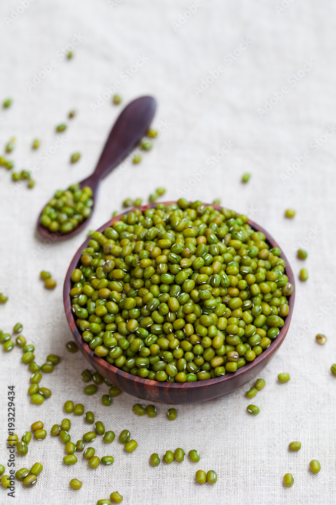 Mung bean, green moong dal in wooden bowl. White textile background. Mung bean, green moong dal in wooden bowl. White textile background.