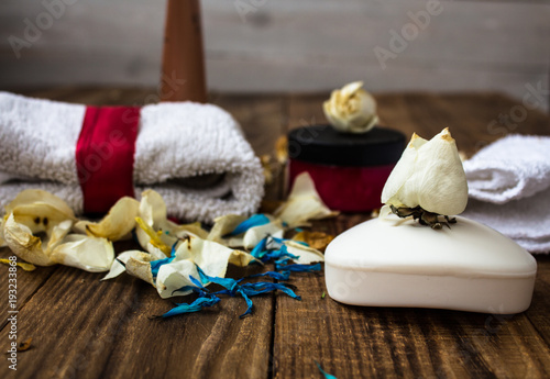 soap and different skin creams with towels and flowers on wooden background