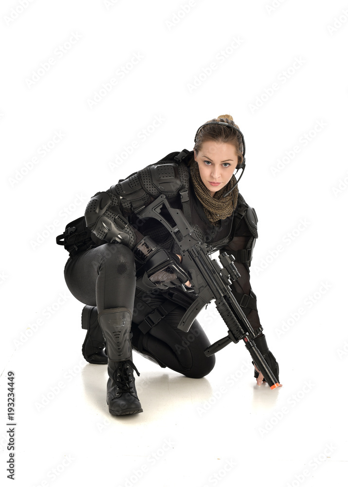 full length portrait of female wearing black tactical armour, crouching pose holding a weapon, isolated on white studio background. full length portrait of female wearing black tactical armour, crouching pose holding a weapon, isolated on white studio background.