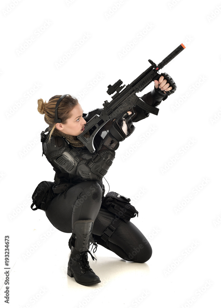 full length portrait of female wearing black tactical armour, crouching pose holding a weapon, isolated on white studio background. full length portrait of female wearing black tactical armour, crouching pose holding a weapon, isolated on white studio background.