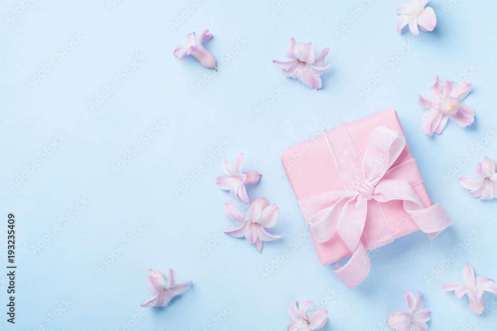 Pink flowers and present or gift box on blue pastel table top view. Greeting card for 8 March, Womans or Mothers Day. Flat lay.