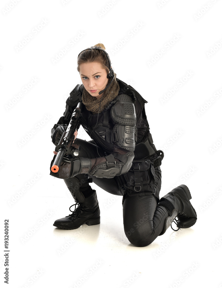 full length portrait of female wearing black tactical armour, crouching pose holding a weapon, isolated on white studio background. full length portrait of female wearing black tactical armour, crouching pose holding a weapon, isolated on white studio background.