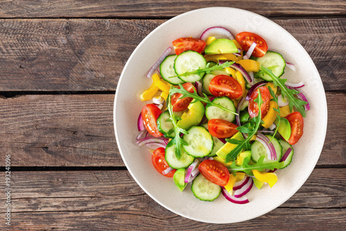 Healthy vegetarian dish, vegetable salad with fresh tomato, cucumber, bell pepper, red onion, avocado and arugula