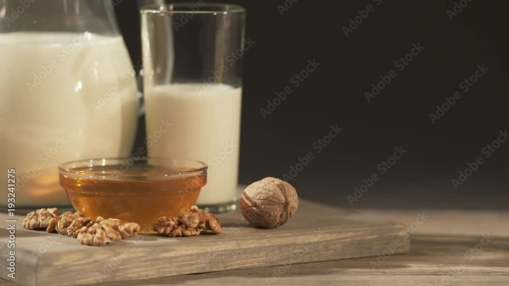 Wedge of Swiss cheese with jug of milk on an old wooden table. Close-up of board with cheese, milk jug, nuts and honey on a dark background. Dolly shot Wedge of Swiss cheese with jug of milk on an old wooden table. Close-up of board with cheese, milk jug, nuts and honey on a dark background. Dolly shot