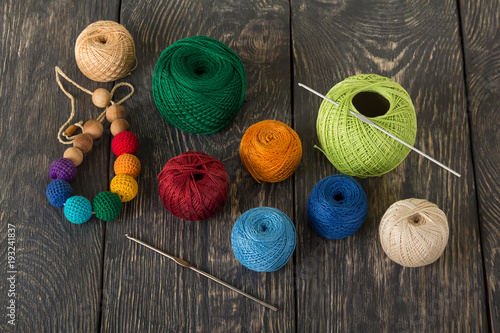 Balls of yarn in different colors and knitting hooks for craft on wooden surface