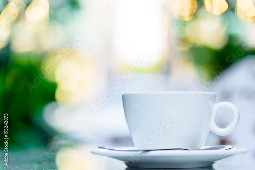 A white cup of coffee and silver spoon ready to served in the morning with relaxing and yellow lighting bokeh background.
