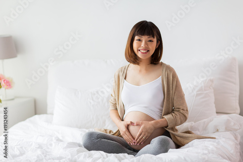 happy pregnant woman making heart gesture in bed