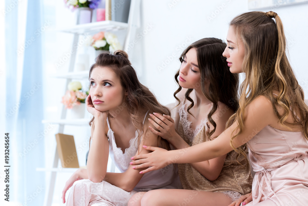 young women in pajamas supporting upset girlfriend while sitting at home young women in pajamas supporting upset girlfriend while sitting at home