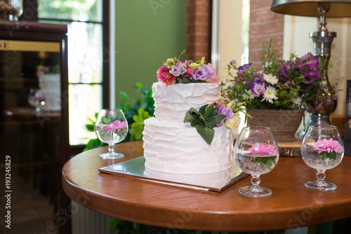 White 2 tiered wedding cake decorated with pink and lilac flowers on the top. Traditional Two Tiered White Wedding Cake with Flowers. Restaurant