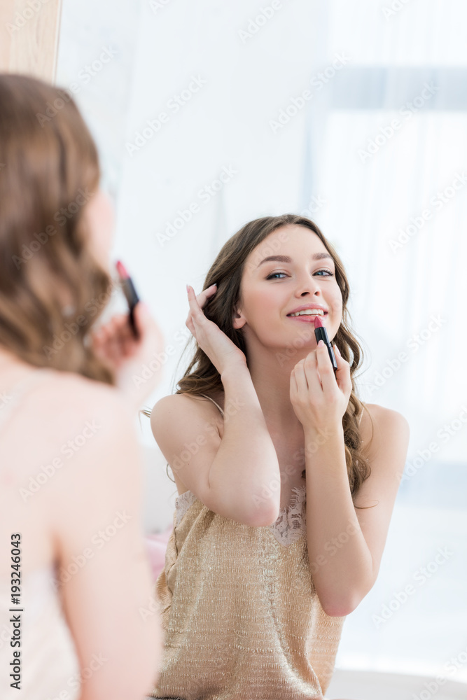 beautiful smiling young woman in lingerie applying lipstick and looking at mirror beautiful smiling young woman in lingerie applying lipstick and looking at mirror