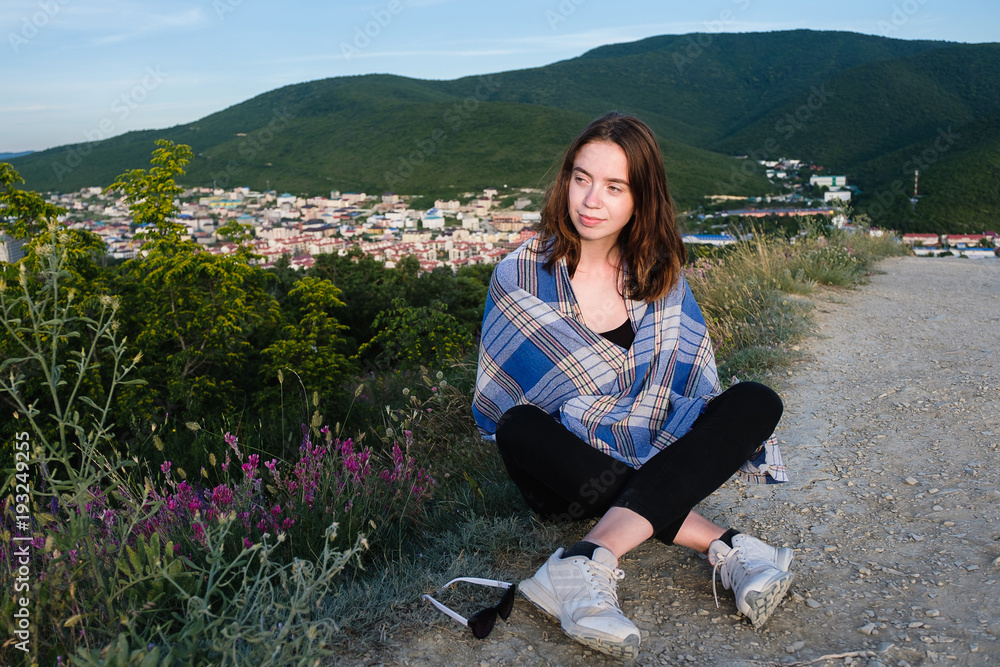 Young girl sits on a mountain, wrapped in a blanket. Cool summer evening in the mountains.