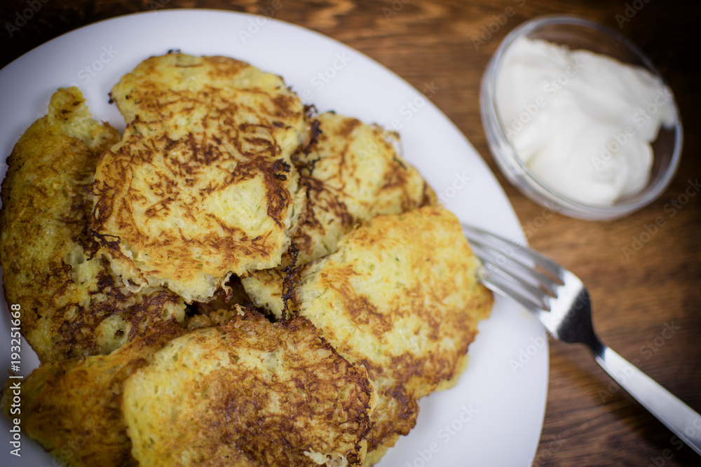 Fried potato pancakes on a white plate and sour cream. Fried potato pancakes on a white plate and sour cream.