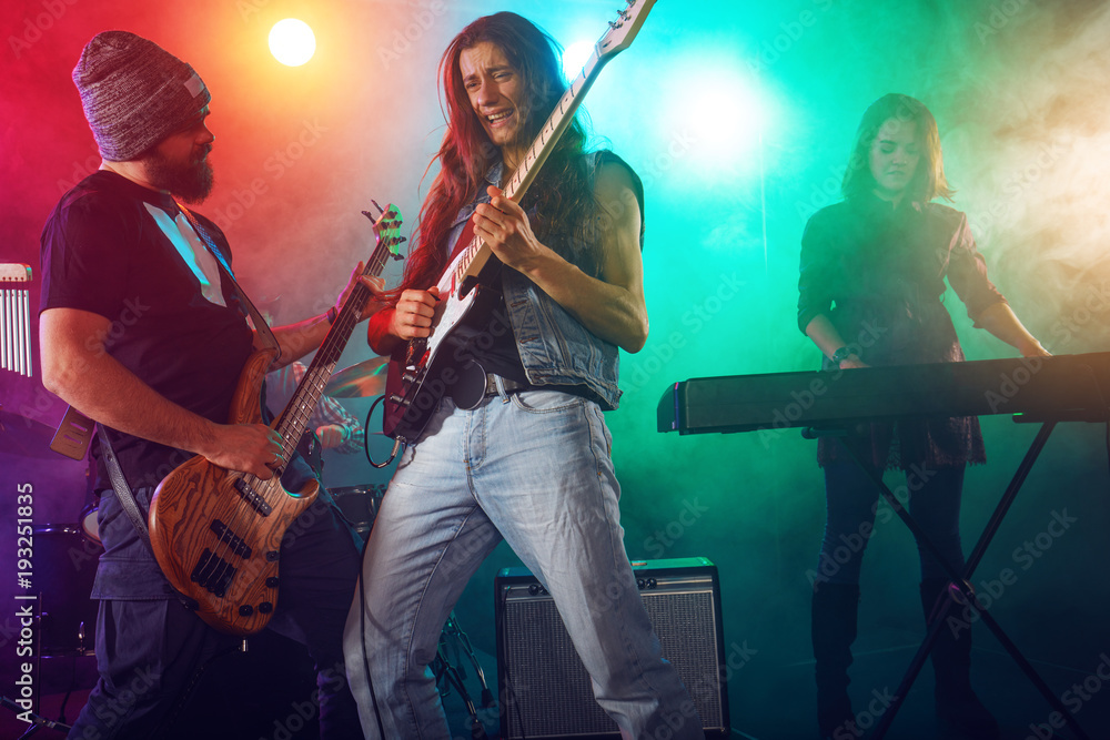 Obraz premium Rock band performs on stage. Guitarist, bass guitar and drums.
