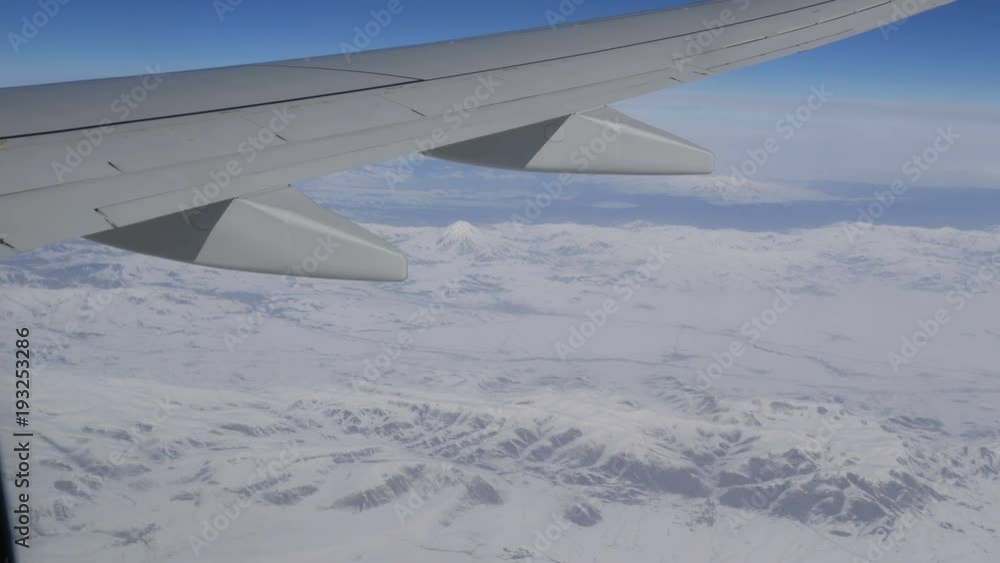 Stunning beauty of the mountain range, slightly covered with snow, passing by clouds, a view from the airplane window Stunning beauty of the mountain range, slightly covered with snow, passing by clouds, a view from the airplane window