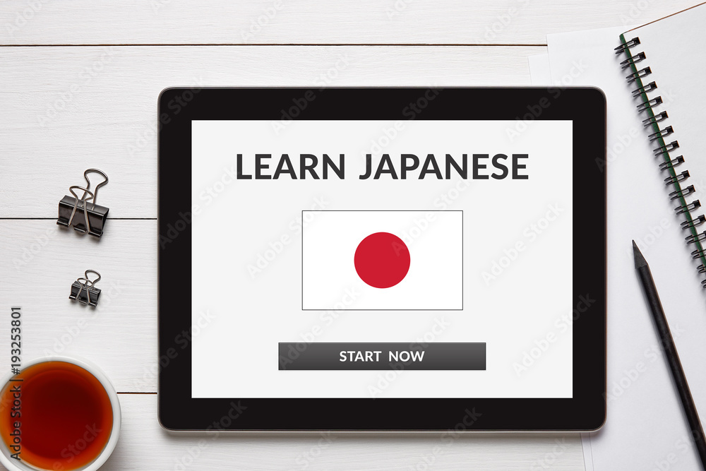 Learn Japanese concept on tablet screen with office objects on white wooden table. All screen content is designed by me. Flat lay Learn Japanese concept on tablet screen with office objects on white wooden table. All screen content is designed by me. Flat lay