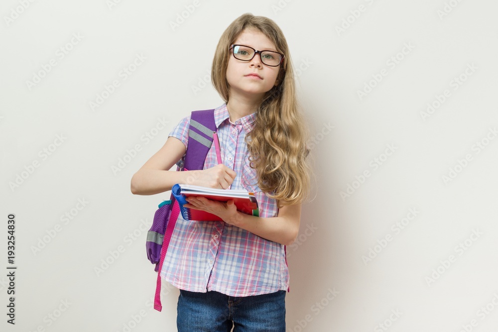 Young schoolgirl in glasses and with a backpack writes in a school notebook. Young schoolgirl in glasses and with a backpack writes in a school notebook.