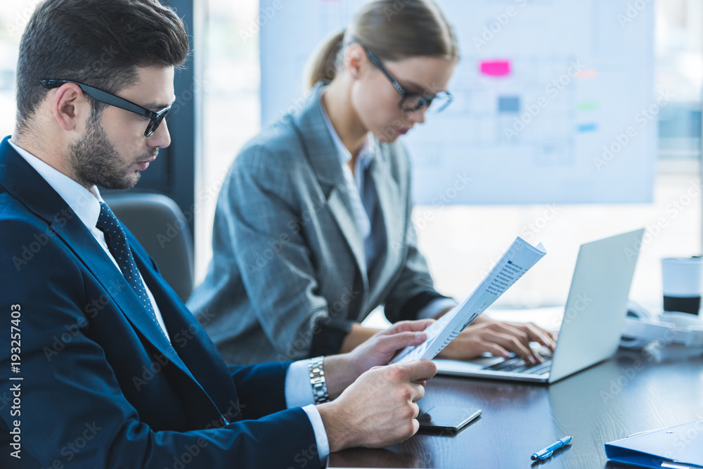 side view of businessman and businesswoman looking at documents in office side view of businessman and businesswoman looking at documents in office