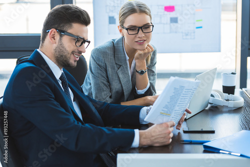 smiling businessman and businesswoman looking at documents in office