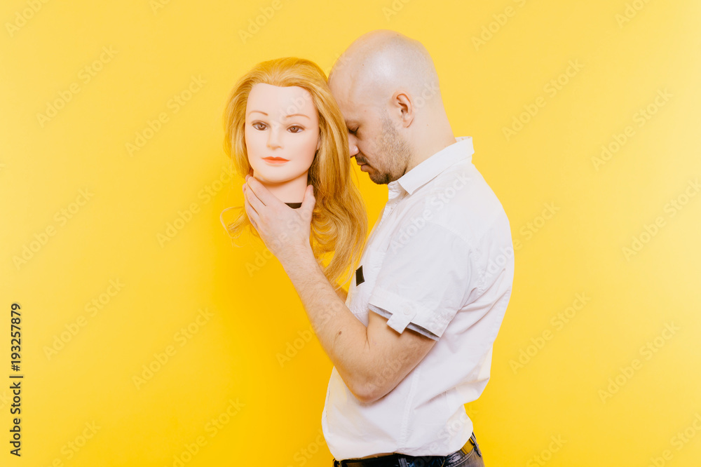 Excited odd bizarre strange unusual sad adult bald hairless man holding plastic blonde woman head. Funny male with girlfriend isolated on yellow. Baldness after chemotherapy. Cancer hair loss concept. Stock Photo | Excited odd bizarre strange unusual sad adult bald hairless man holding plastic blonde woman head. Funny male with girlfriend isolated on yellow. Baldness after chemotherapy. Cancer hair loss concept. Stock Photo |