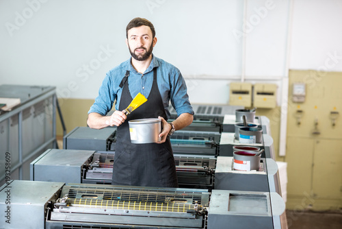 Portrait of a handsome typographer standing with yellow paint for offset machine at the printing manufacturing