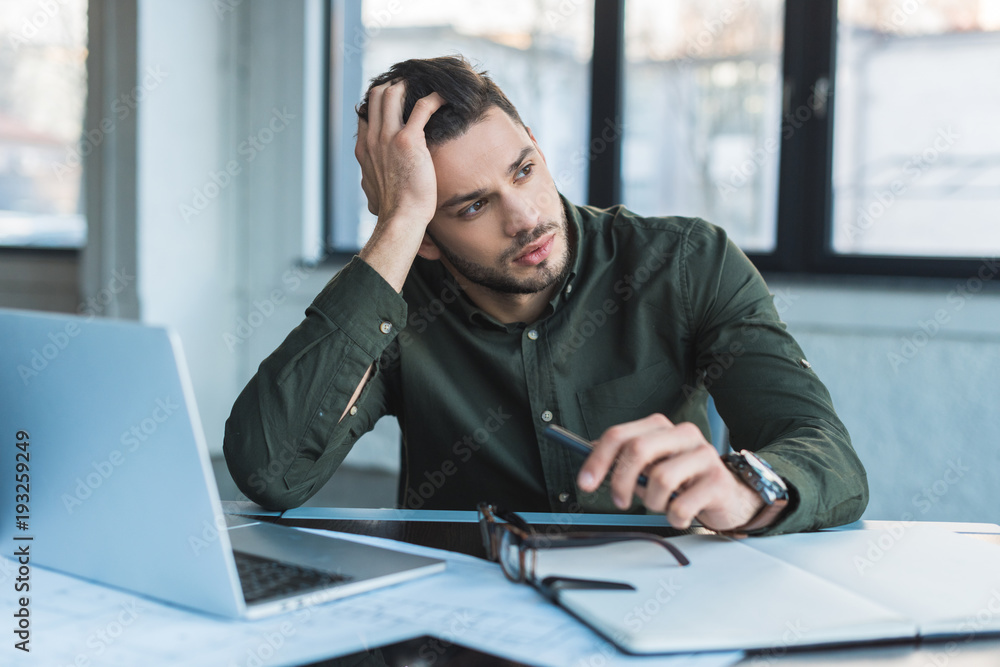 handsome businessman sitting at table in office and looking away handsome businessman sitting at table in office and looking away