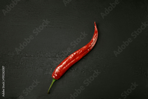 Red chili pepper on a black slate plate. Hot pepper of red color in the center of the frame.